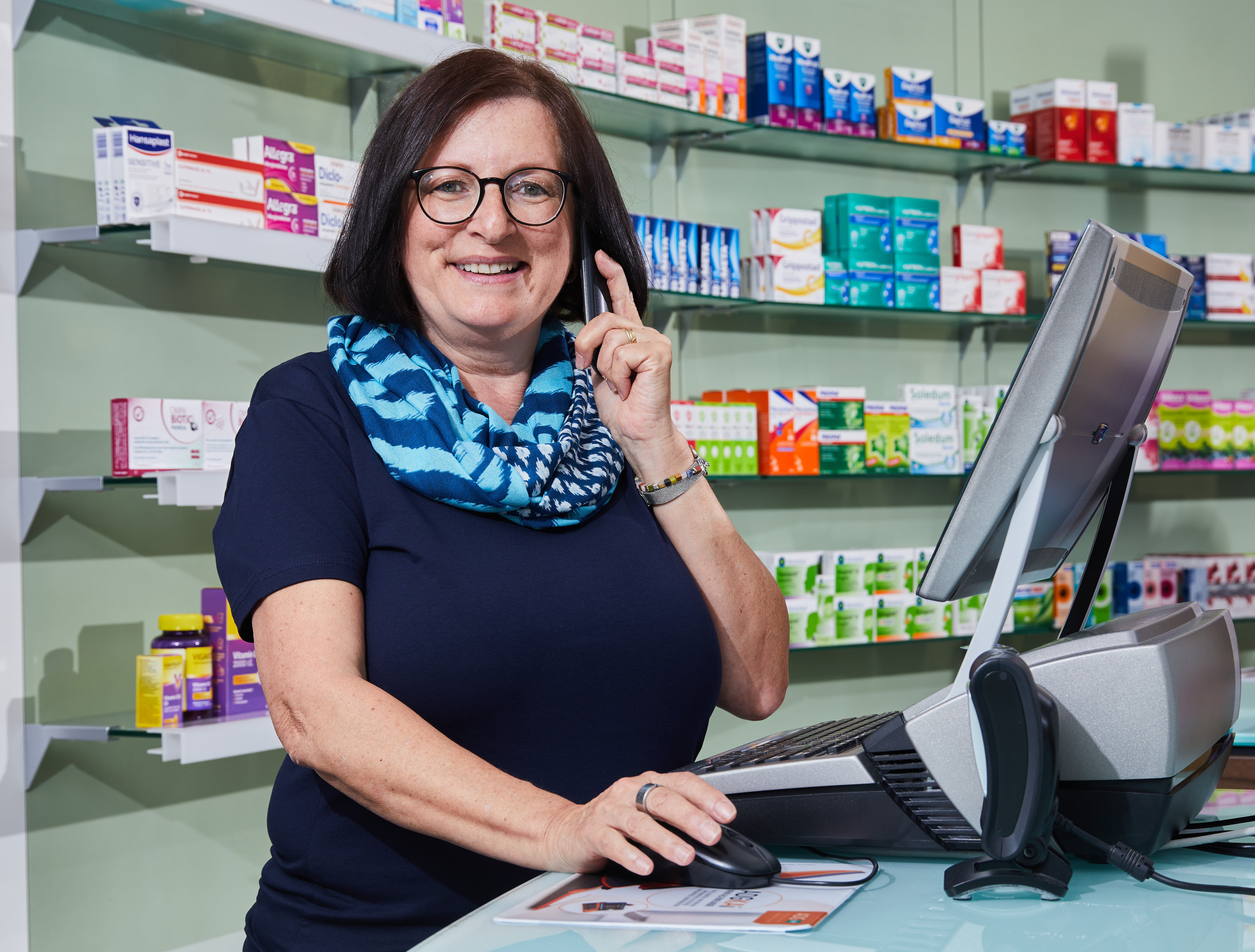 Moderne Innenansicht der Löwen-Apotheke, Apothekerin steht am PC und telefoniert.